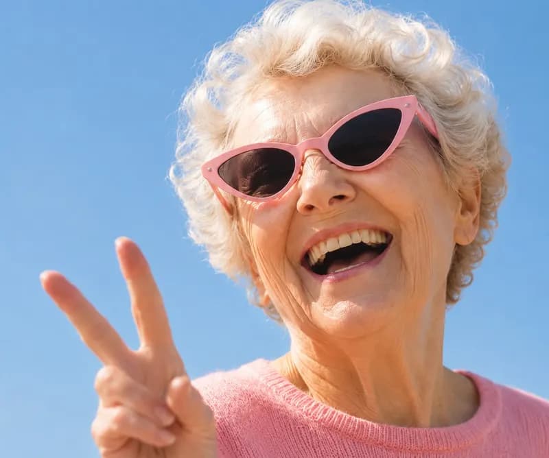 Une aînée rit, lunettes roses, en faisant le signe de la paix